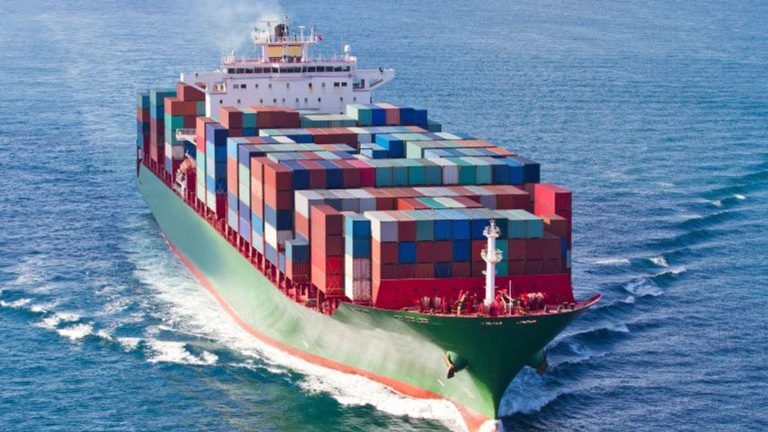 A large cargo ship filled with colorful containers sails on the ocean.