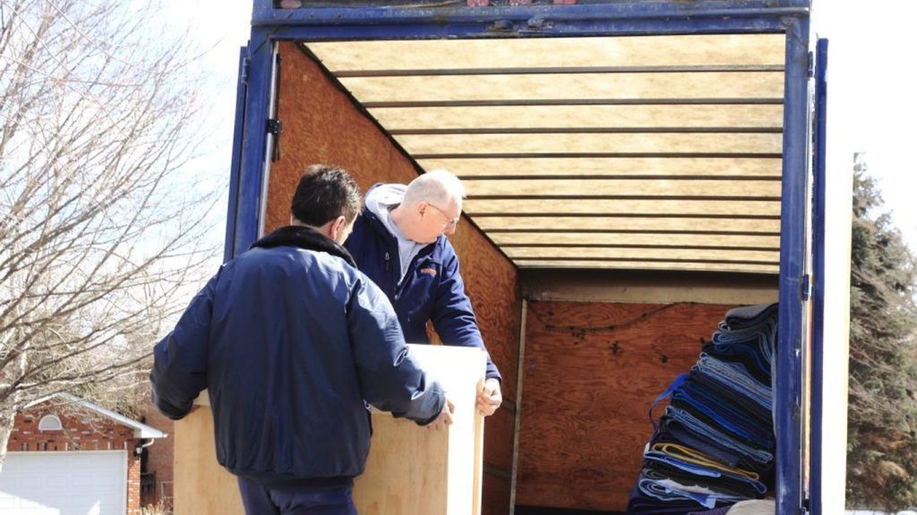 Two people loading a large wooden object into a truck.